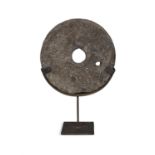 A FLAT CIRCULAR LIMESTONE QUERN STONE, with pierced centre on steel stand. 68cm high, 45cm wide,