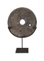 A FLAT CIRCULAR LIMESTONE QUERN STONE, with pierced centre on steel stand. 68cm high, 45cm wide,