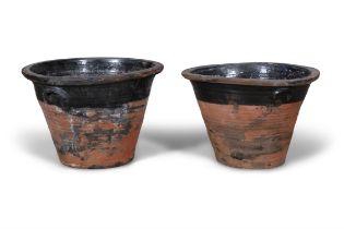 A PAIR OF TERRACOTTA MILK CROCKS, the moulded rim above black glazed body with thrown handles.