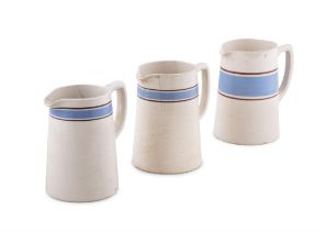 A SET OF THREE CARRIGALINE POTTERY JUGS in various sizes, with a large mug, plain cream with