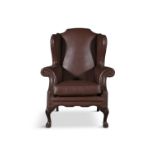 A MAHOGANY FRAMED WINGBACK ARMCHAIR, upholstered in a brown hide, on leaf capped cabriole legs