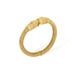 A 22K GOLD BANGLE Of spring design, each terminal with opposing stylised Chimera heads, to a