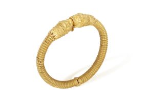 A 22K GOLD BANGLE Of spring design, each terminal with opposing stylised Chimera heads, to a