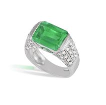 AN EMERALD AND DIAMOND DRESS RING Horizontally-set, the cut-cornered rectangular emerald weighing