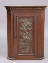 A 19th century oak hanging corner cupboard fitted centre shelf enclosed by a carved floral panel