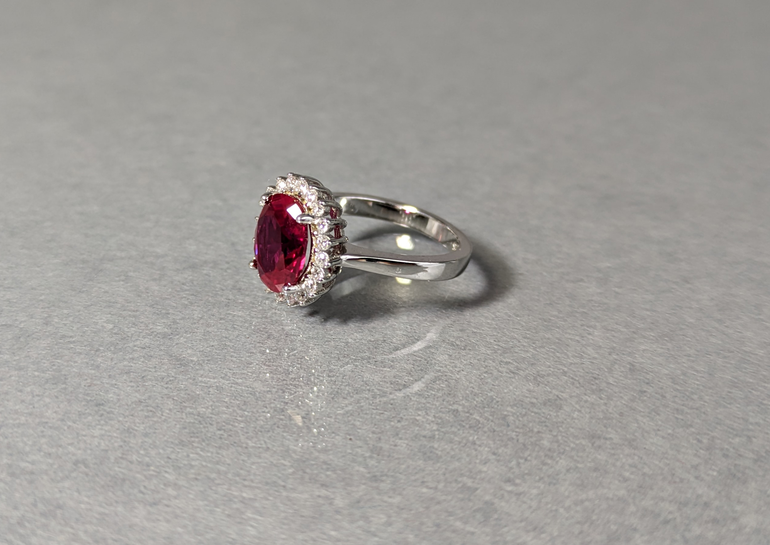A dress ring set oval-cut cubic zirconium of deep red colour, within a border of small white stones, - Image 2 of 3