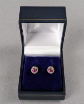 A pair of ruby & diamond ear studs, each round-cut ruby set within a border of rose diamonds to