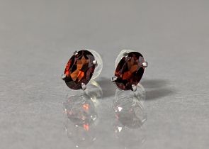 A pair of garnet ear-studs, the oval-cut stones set to 10k white mounts.