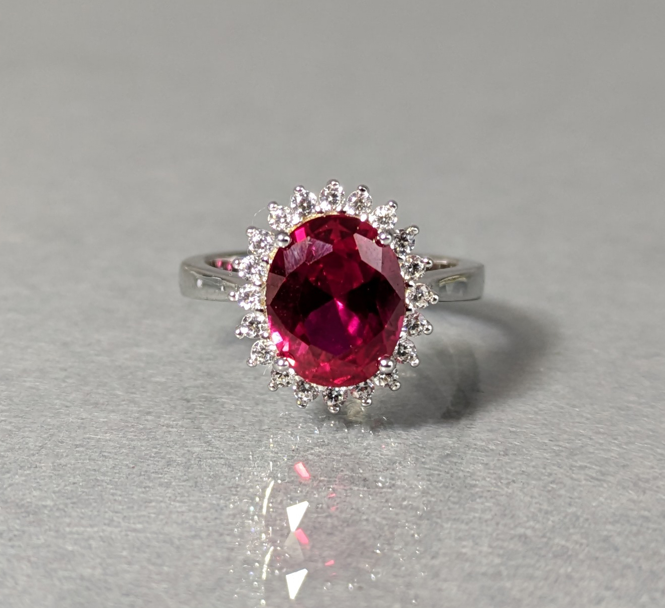 A dress ring set oval-cut cubic zirconium of deep red colour, within a border of small white stones,