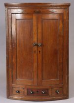 A George III oak bow-front hanging corner cupboard with three shelves enclosed by pair of fielded