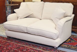 A Howard-style two-seater settee with a square back, shaped arms & with loose cushions upholstered
