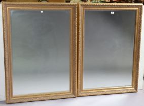 A pair of gilt frame rectangular wall mirrors each with a raised scroll border & inset with a