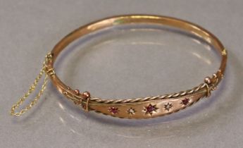 An Edwardian 9ct gold stiff hinged bangle set three small graduated rubies with tiny rose diamonds