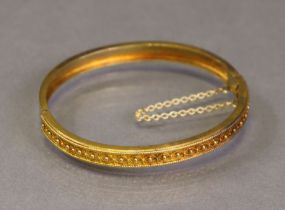 A 15ct gold stiff-hinged bangle with safety chain, one half decorated with applied bead-&-loop
