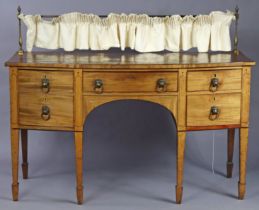 A Regency mahogany bow-front sideboard fitted four drawers with brass lion-mask handles, on six