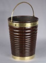 A George III Irish mahogany peat bucket of ribbed & tapered form with brass mounts and swing handle,