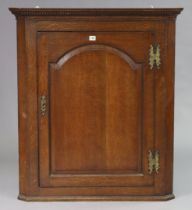 A 19th century oak hanging corner cabinet fitted three shaped shelves enclosed by a fielded panel
