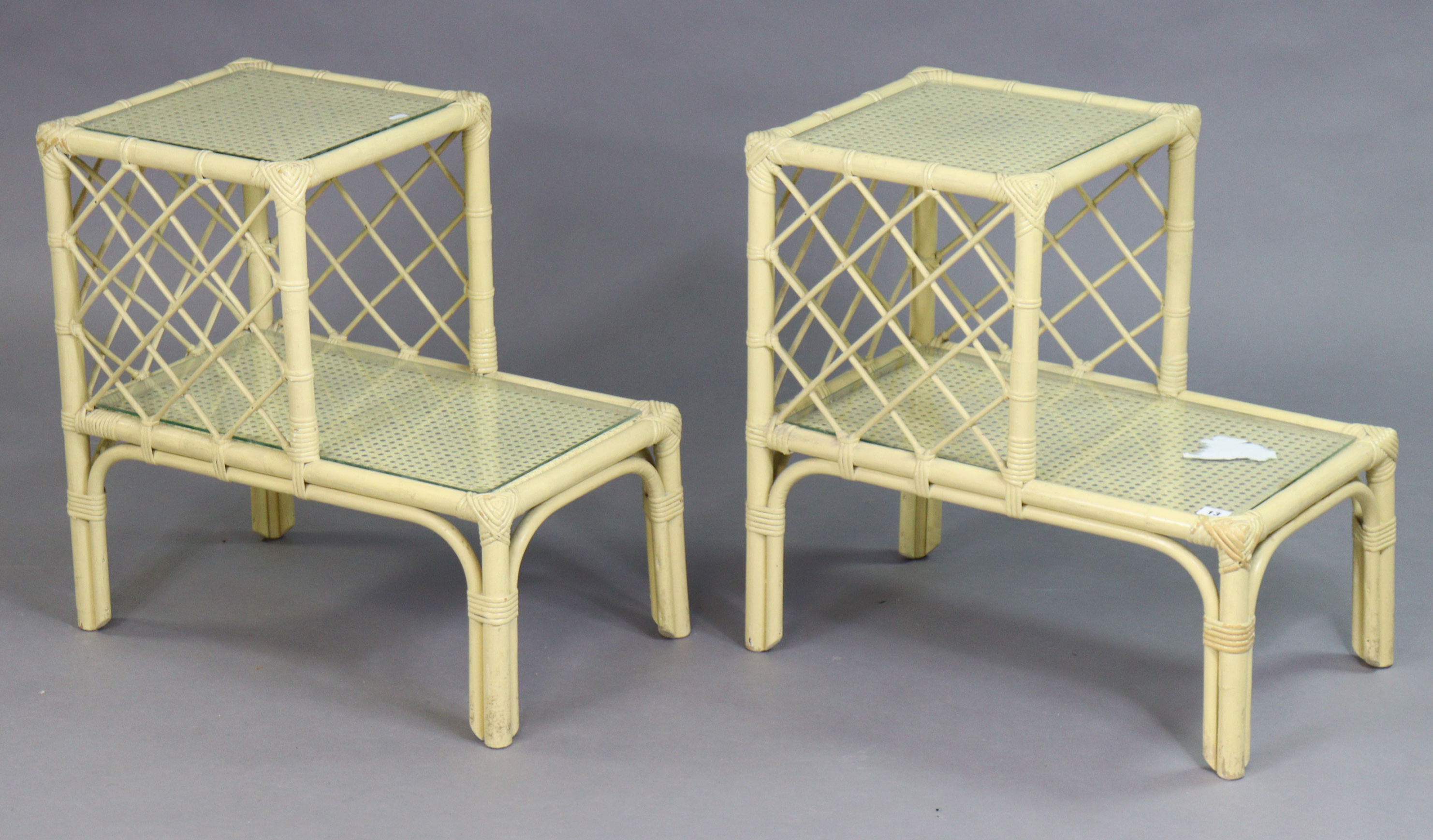 A pair of cream-painted wicker & cane two-tier occasional tables, each inset glass tops.
