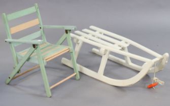 A white painted wooden child’s sledge, 83cm long, and a child’s fold-away chair.