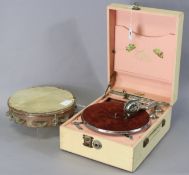 A Ridgmount portable gramophone in a cream finish fibre-covered case; together with a tambourine.