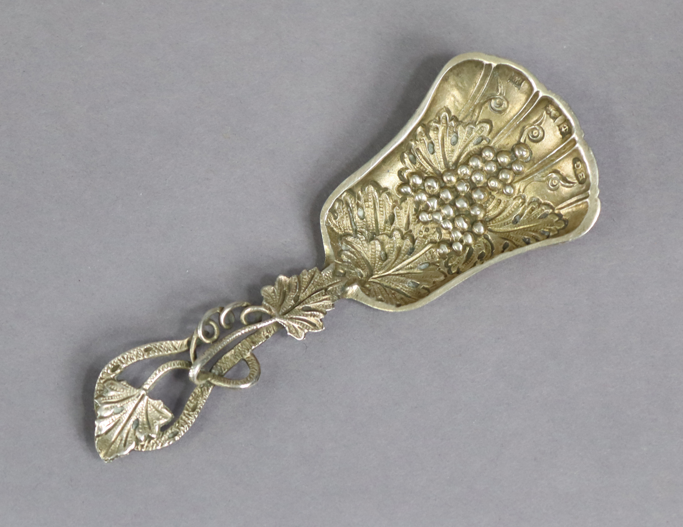 An Elizabeth II silver caddy spoon with a pierced foliate handle, & with raised grapevine design