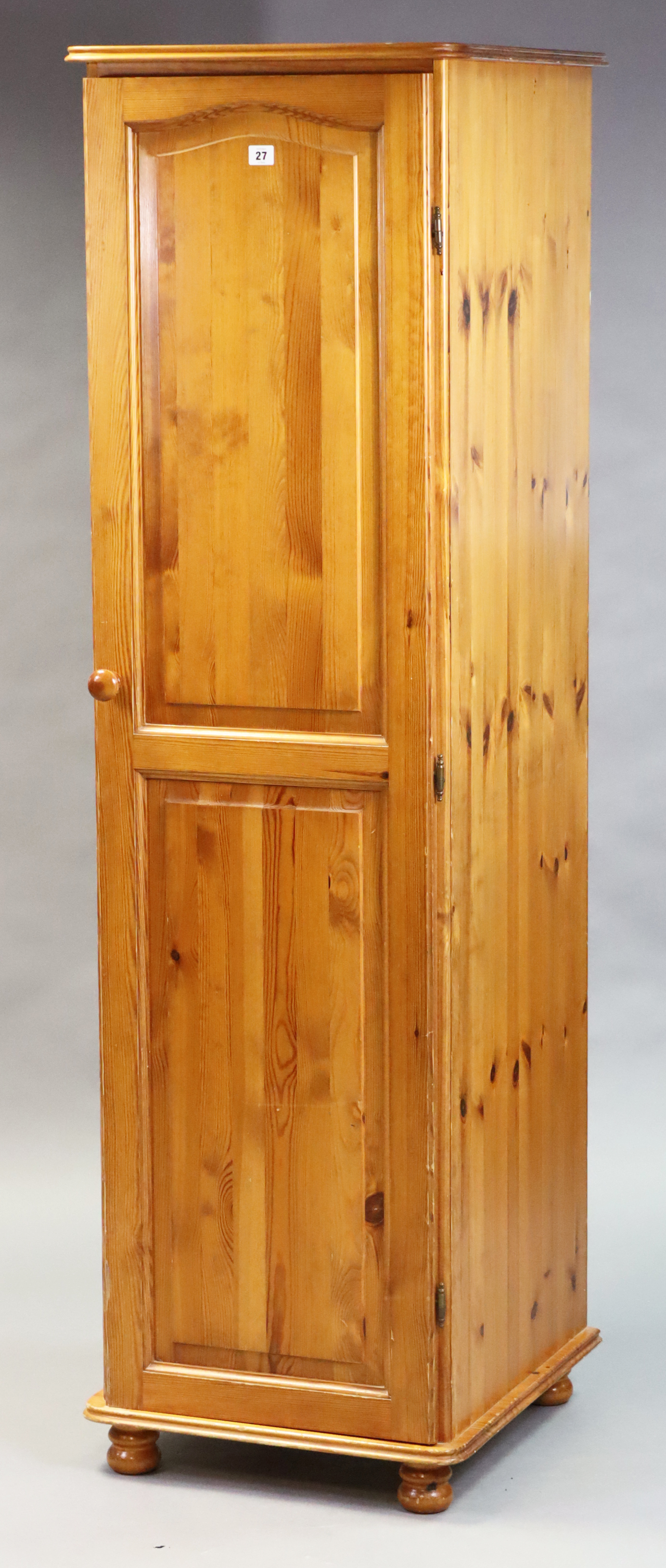 A pine narrow wardrobe enclosed by a fielded panel door, & on bun feet, 50cm wide x 175.5cm high x