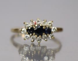 A 9ct. gold ring set three small, graduated sapphires within border of small white stones, size: