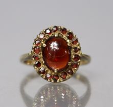A 9ct. gold ring set oval cabochon garnet within a border of small round-cut garnets; size: M; 2.