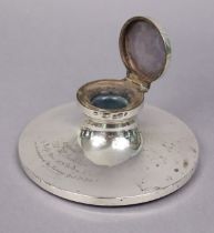 A George V silver capstan inkwell with hinged cover & engraved inscription, 16.3cm dia.;