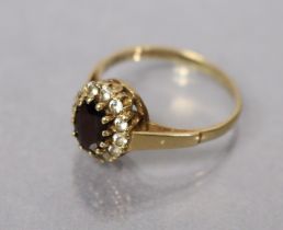 A 9ct. gold ring set oval garnet within a border of small white stones, size: N; 2.1gm.