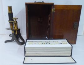 An early 20thC brass microscope with a collection of slides, in a mahogany case