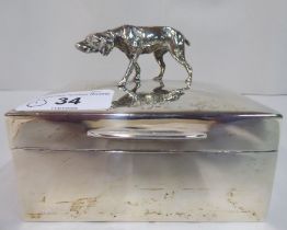 A silver cigarette box with straight sides and a hinged lid, surmounted by a gun dog finial