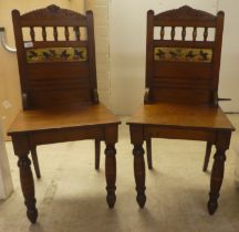 A pair of Edwardian oak hall chairs, the solid seats raised on ring turned forelegs