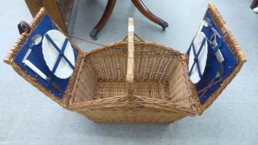 A modern wicker picnic basket, containing two place settings of cutlery and flatware