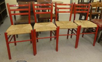 A set of four red stained beech framed kitchen chairs, each with a rush seat, raised on turned legs