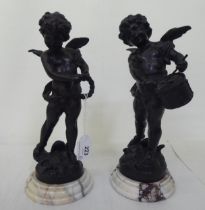 A pair of bronze cherubic figures, posing with instruments, each raised on a marble plinth  bears