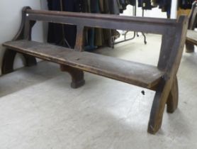 A pair of late 19thC stained pine chapel pews with level, bar backs and solid seats, raised on