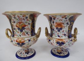 A pair of early 19thC Derby porcelain, twin handled, pedestal urns, decorated in a version of an