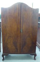 A 1930s walnut finished compactum with an arched top, enclosed by a pair of full height doors,