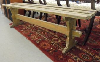 A pine bench of slatted construction, raised on trestle ends  70"L