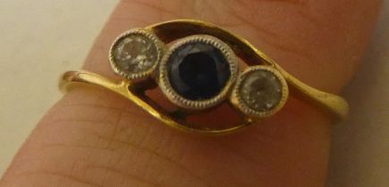 A yellow metal ring, set with two diamonds and a sapphire, in a crossover setting  stamped 18k