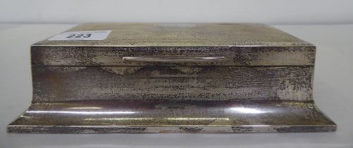 A silver cigarette box of sarcophagus form with engine turned decoration on the hinged lid,