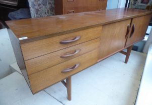 An Avalon teak sideboard with a bank of three offset drawers and a pair of adjacent sliding doors,