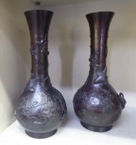 A pair of early 20thC Japanese cast bronze bottle vases with narrow necks and flared rims, decorated