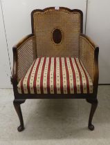 An Edwardian mahogany framed bergere style, enclosed arm chair with woven cane panels, raised on