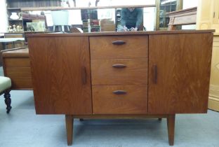 A 1970s teak sideboard, comprising three offset short drawers, flanked by a pair of cupboard doors