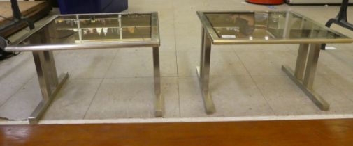 A pair of 1970s brushed stainless steel framed coffee tables with smoked glass tops, raised on