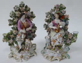 A pair of late 18thC Derby porcelain figures, a man seated with a dog, before a bocage and playing