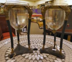 A pair of black painted steel and brass vase stands, in neo-classical taste with clear glass liners,