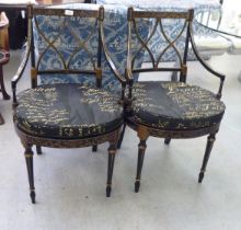 A pair of modern Regency design black and gold painted chairs with a crossover backs, raised on